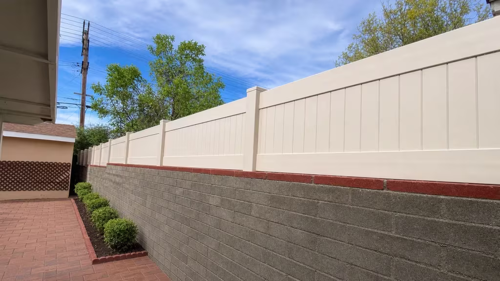 Rear lattice structure stands beside a White vinyl privacy wall topper mounted on the red masonry cap course