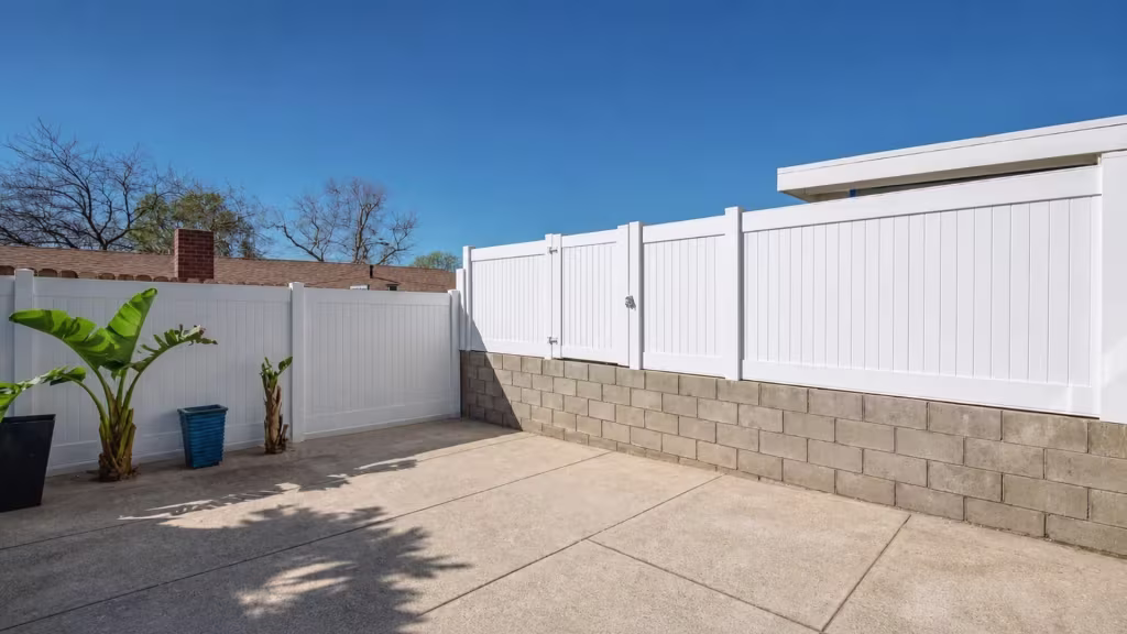 Banana plants line a patio corner where the White vinyl privacy wall topper shifts from block wall to fence panels