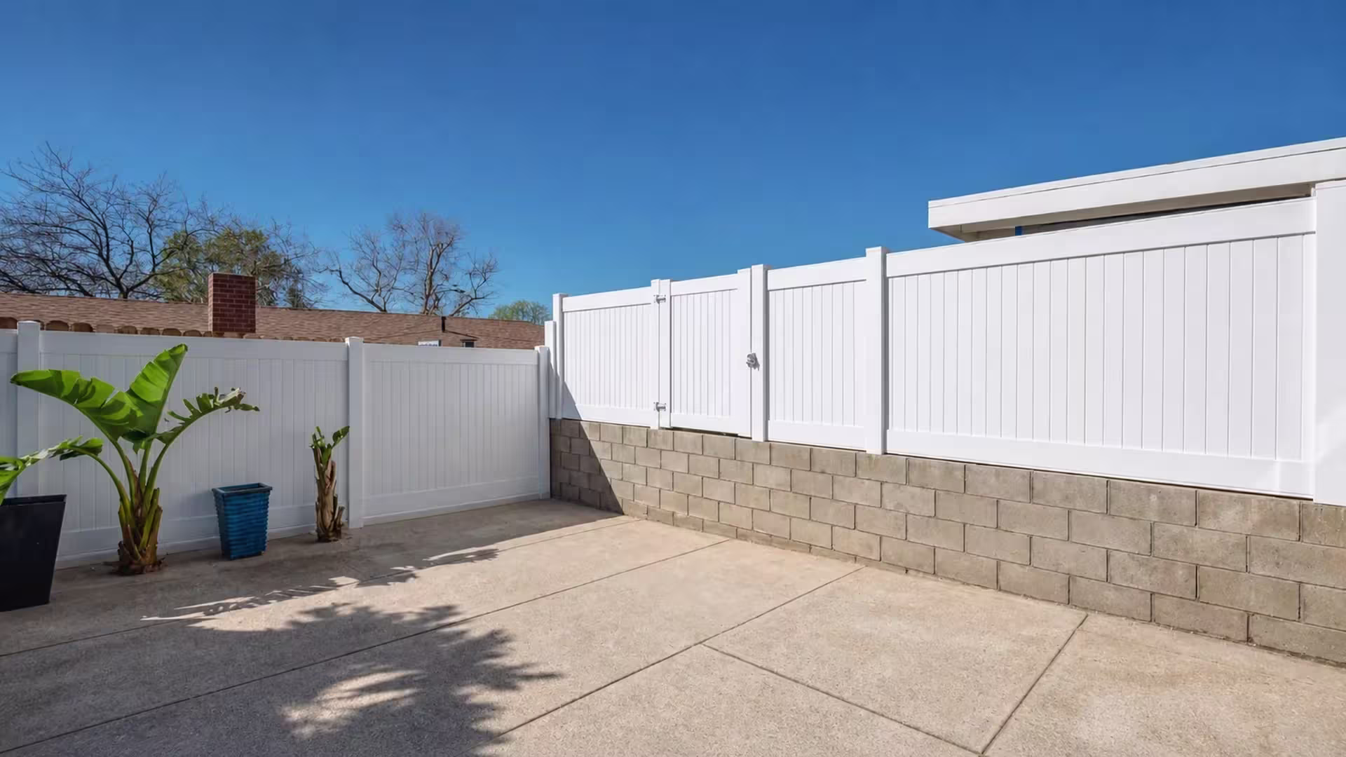 Banana plants line a patio corner where the White vinyl privacy wall topper shifts from block wall to fence panels
