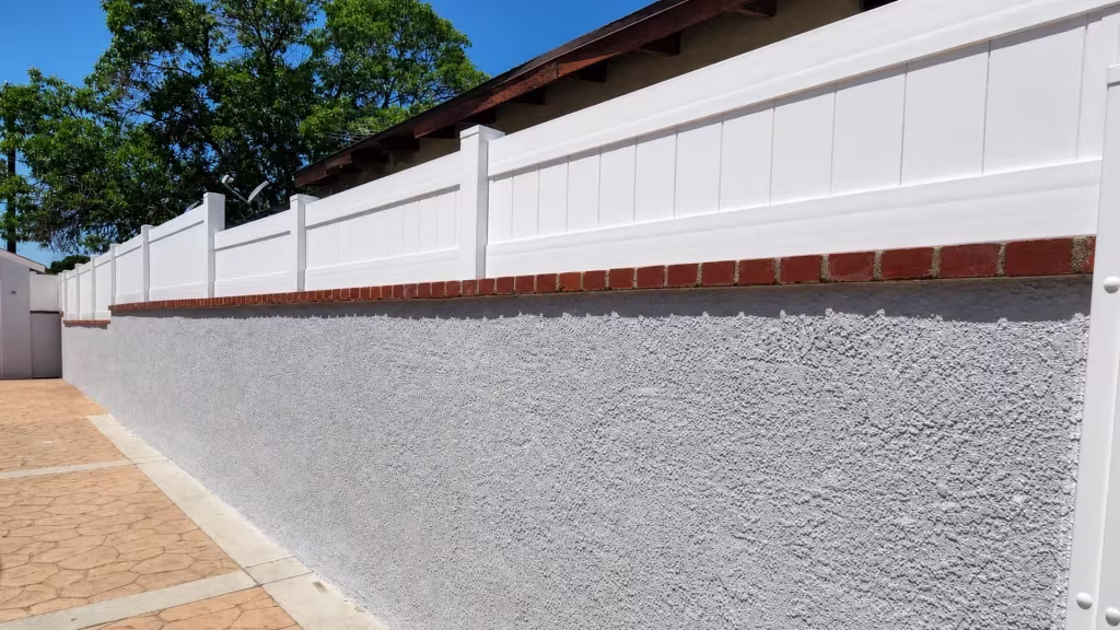 White vinyl privacy wall topper runs the red brick cap of a tall textured stucco masonry wall