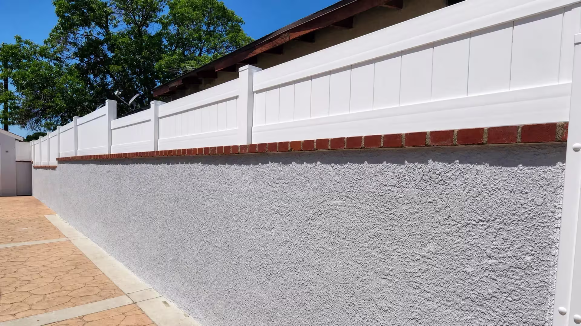 White vinyl privacy wall topper runs the red brick cap of a tall textured stucco masonry wall