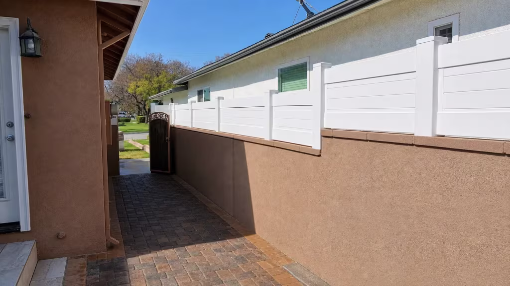 Stucco-lined side passage carries a White vinyl privacy wall topper toward a distant gate at the property line