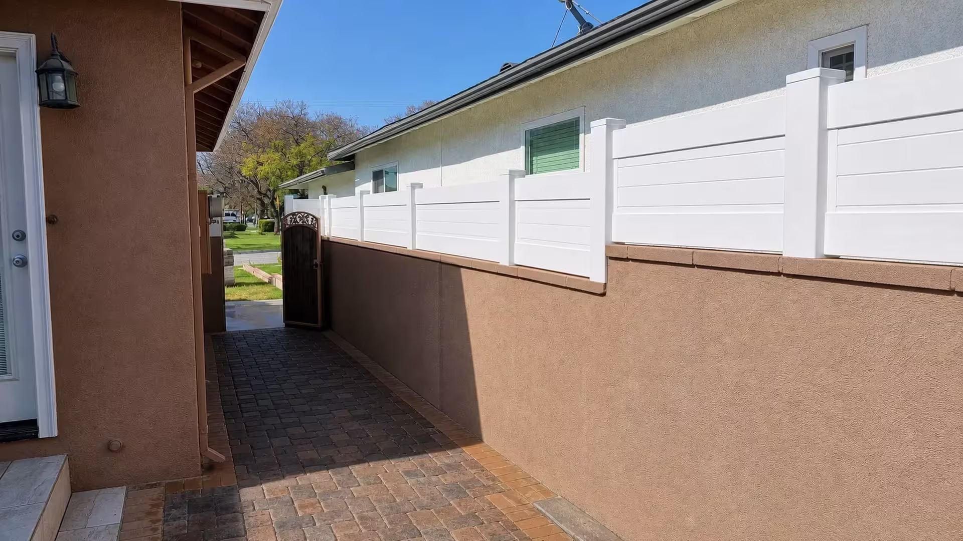 Stucco-lined side passage carries a White vinyl privacy wall topper toward a distant gate at the property line