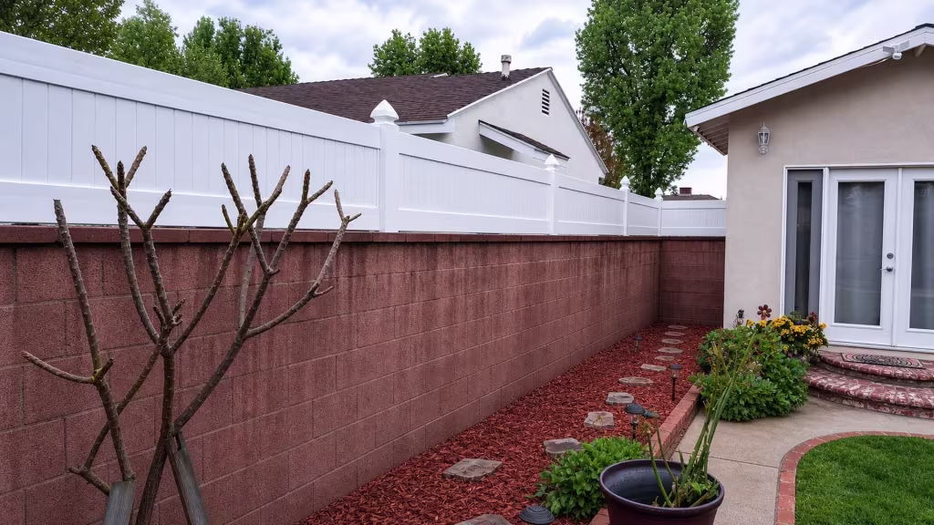 Patio doors and brick-edged garden steps sit near a White vinyl privacy wall topper capping the red-brown block wall