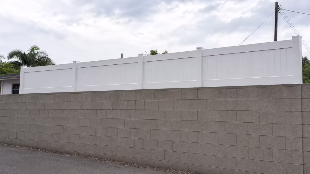 Palm fronds and overhead utility wires overhang a White vinyl privacy topper rising with the graded block wall