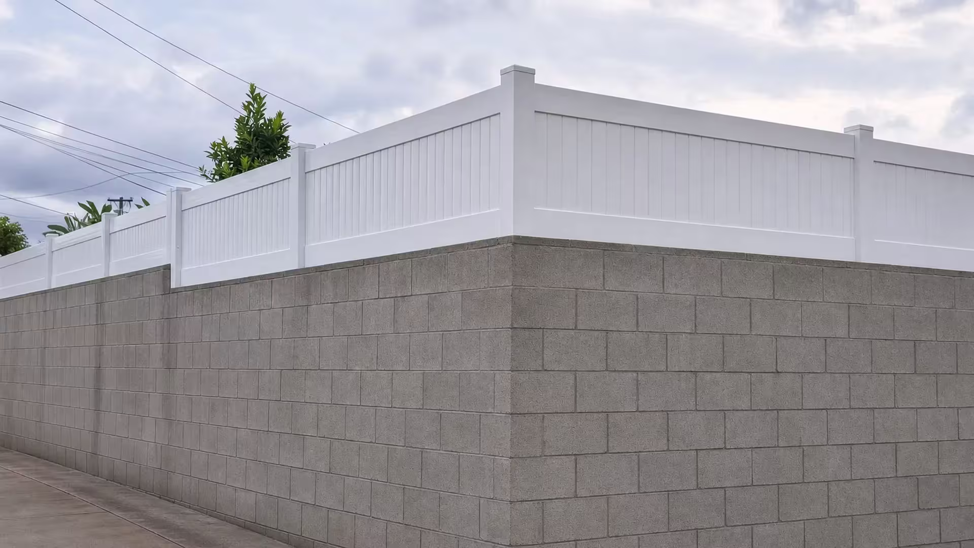A square outside corner catches the White vinyl privacy topper as it wraps a tall gray block wall along the alley