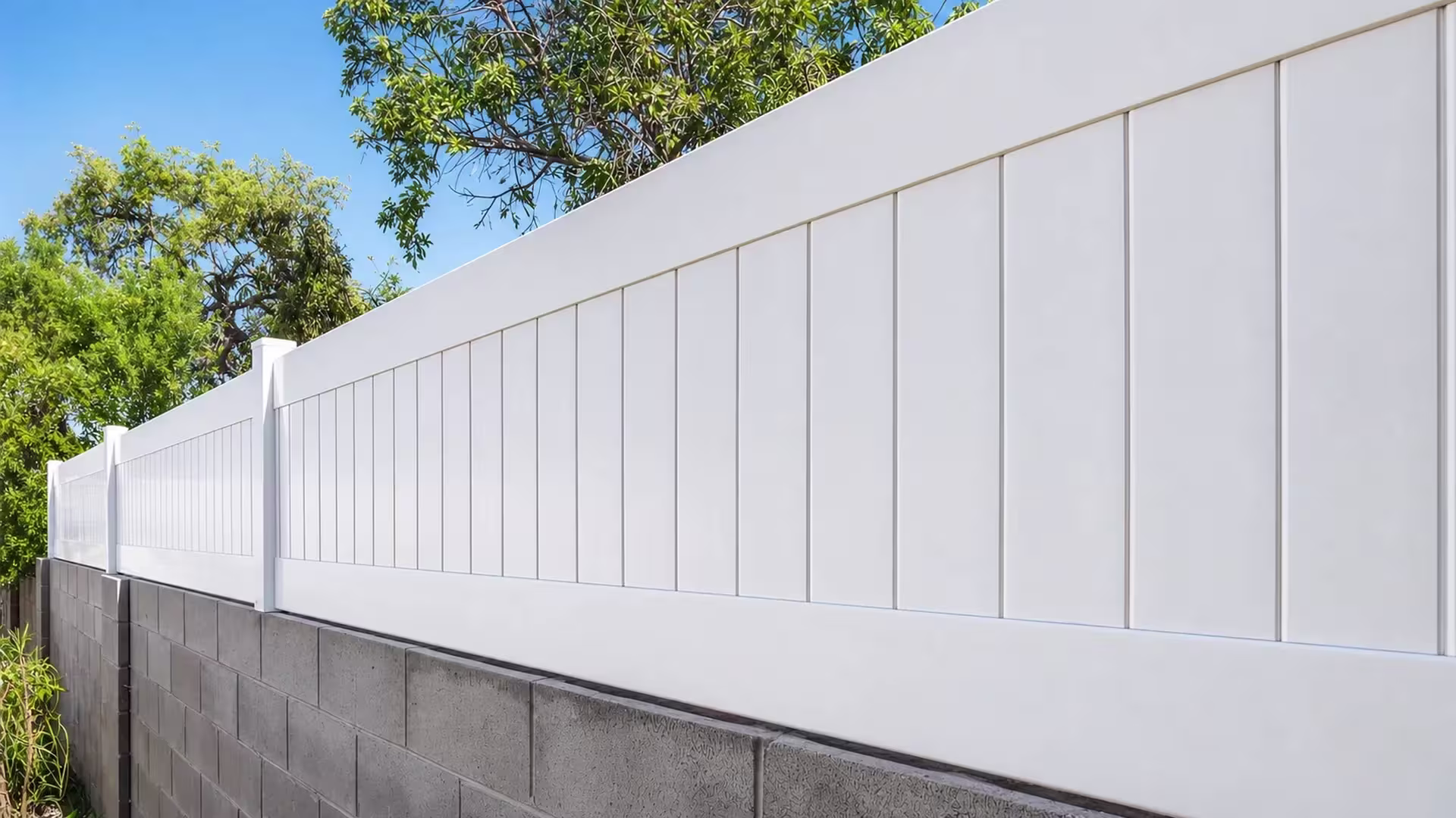 Continuous White vinyl wall topper follows a mortared block wall lined with mature tree trunks and foliage