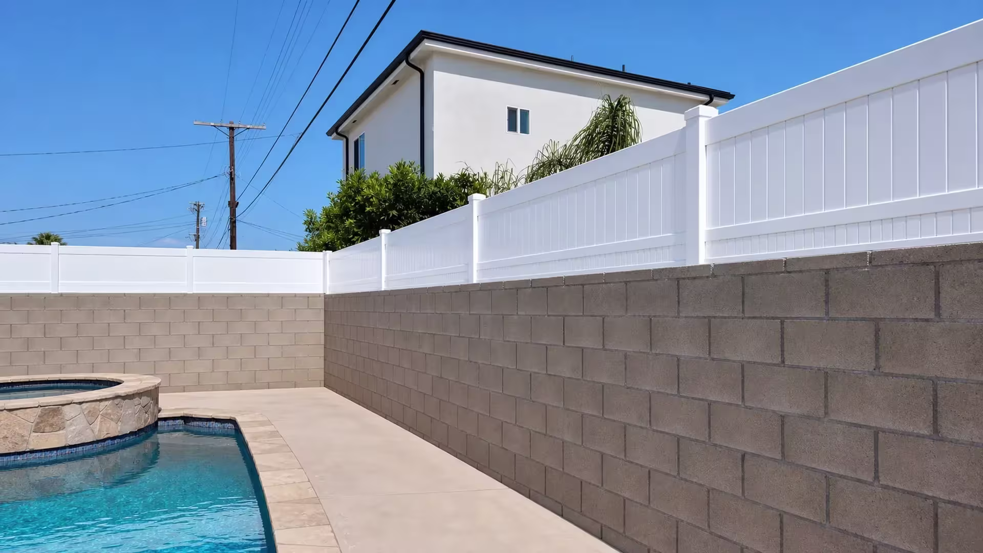 An L-shaped corner carries the White vinyl privacy topper around a block wall bordering this pool deck and coping