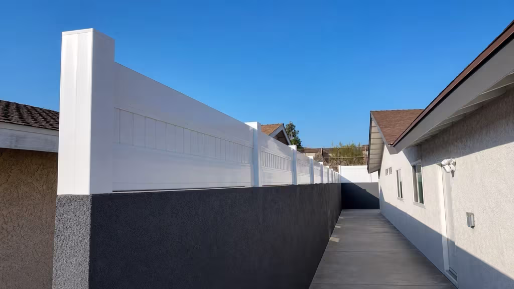 Square posts recede along a charcoal block wall beside the concrete side walkway, each one capped by the White vinyl topper
