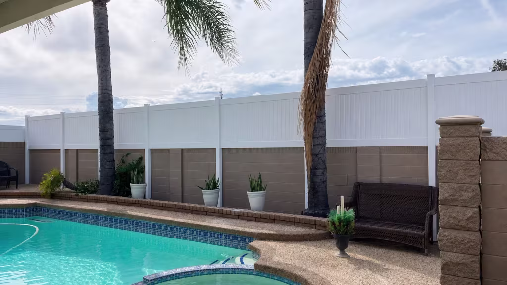 Six panel bays of White vinyl privacy topper span the tan block wall enclosing this backyard