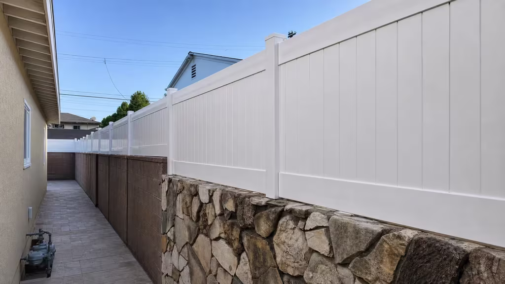 White vinyl privacy topper lines a paved walkway passage beside a building wall and overhanging eaves