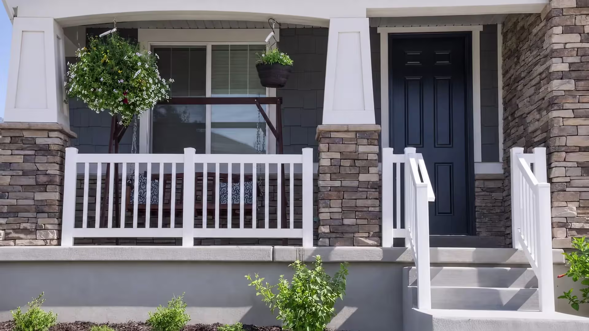White vinyl porch guardrail with two railing bays set between stacked stone piers near a porch swing