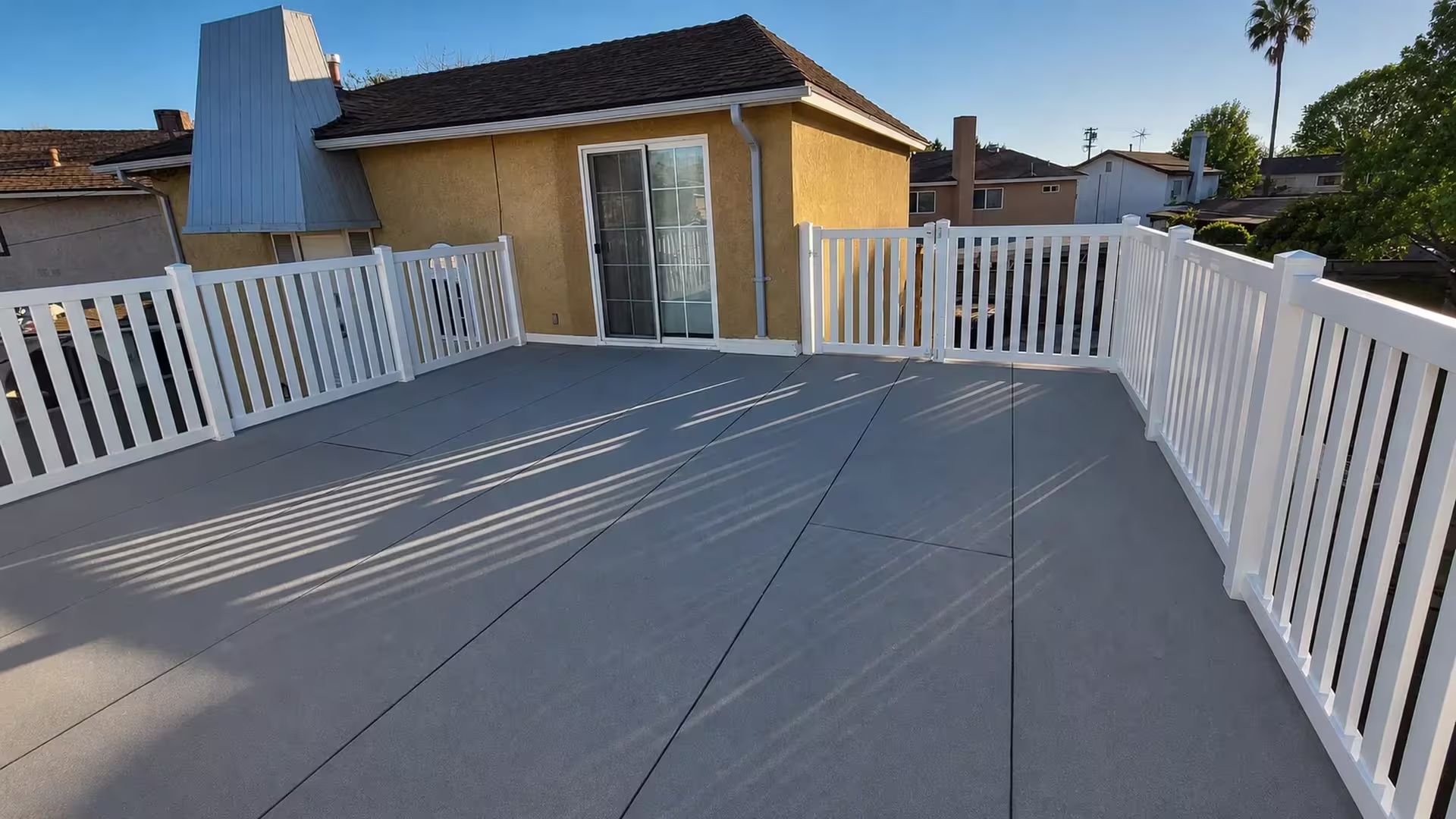 White vinyl picket railing wraps a rooftop deck beside a tan stucco house and sliding glass door