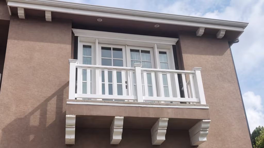 White vinyl balcony railing sits below multi pane glazed doors on a tan stucco facade