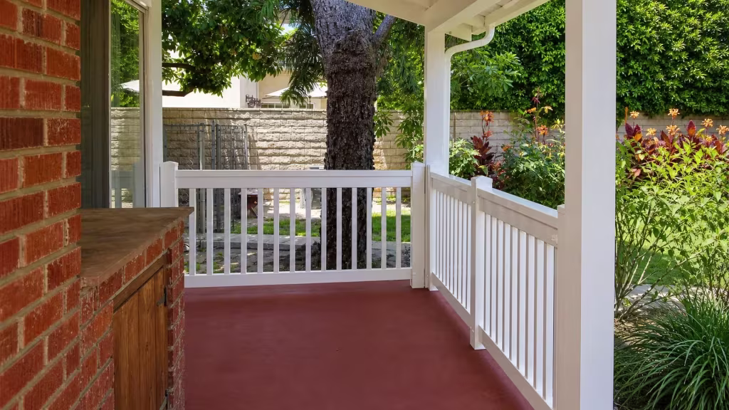 Near a brick wall and a built in wood cabinet, White vinyl porch railing turns a right angle corner
