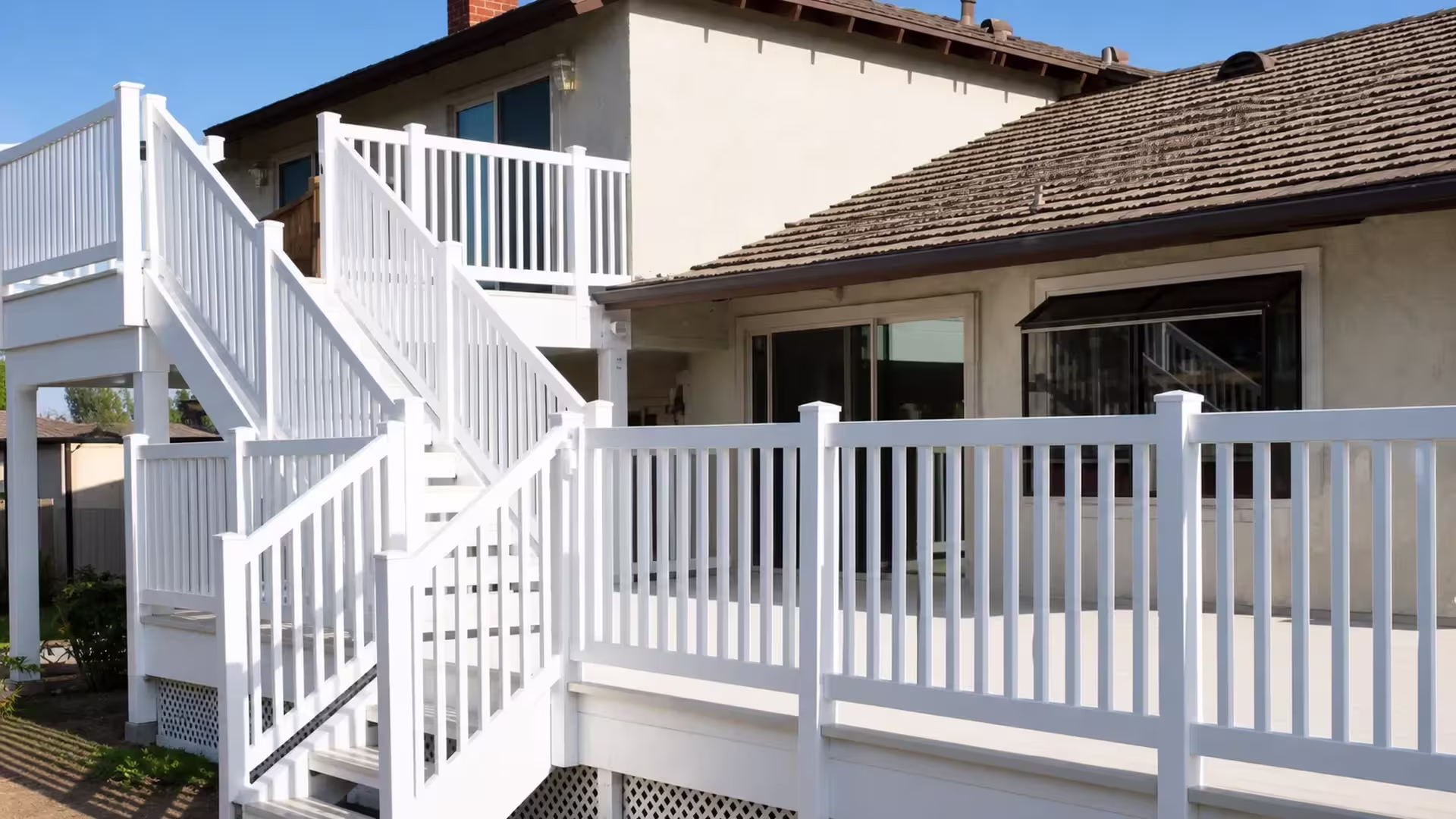 White vinyl deck railing forms several connected runs against a two story stucco house wall