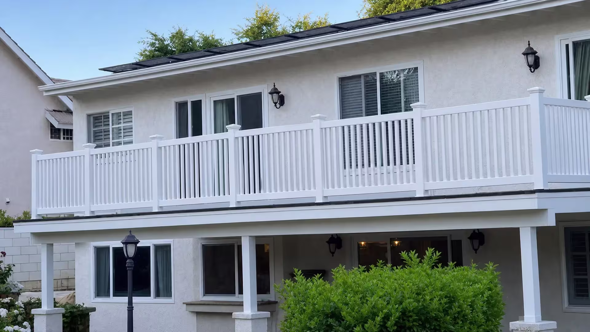 White vinyl balcony railing spans four bays between five posts on a stucco house before turning a corner