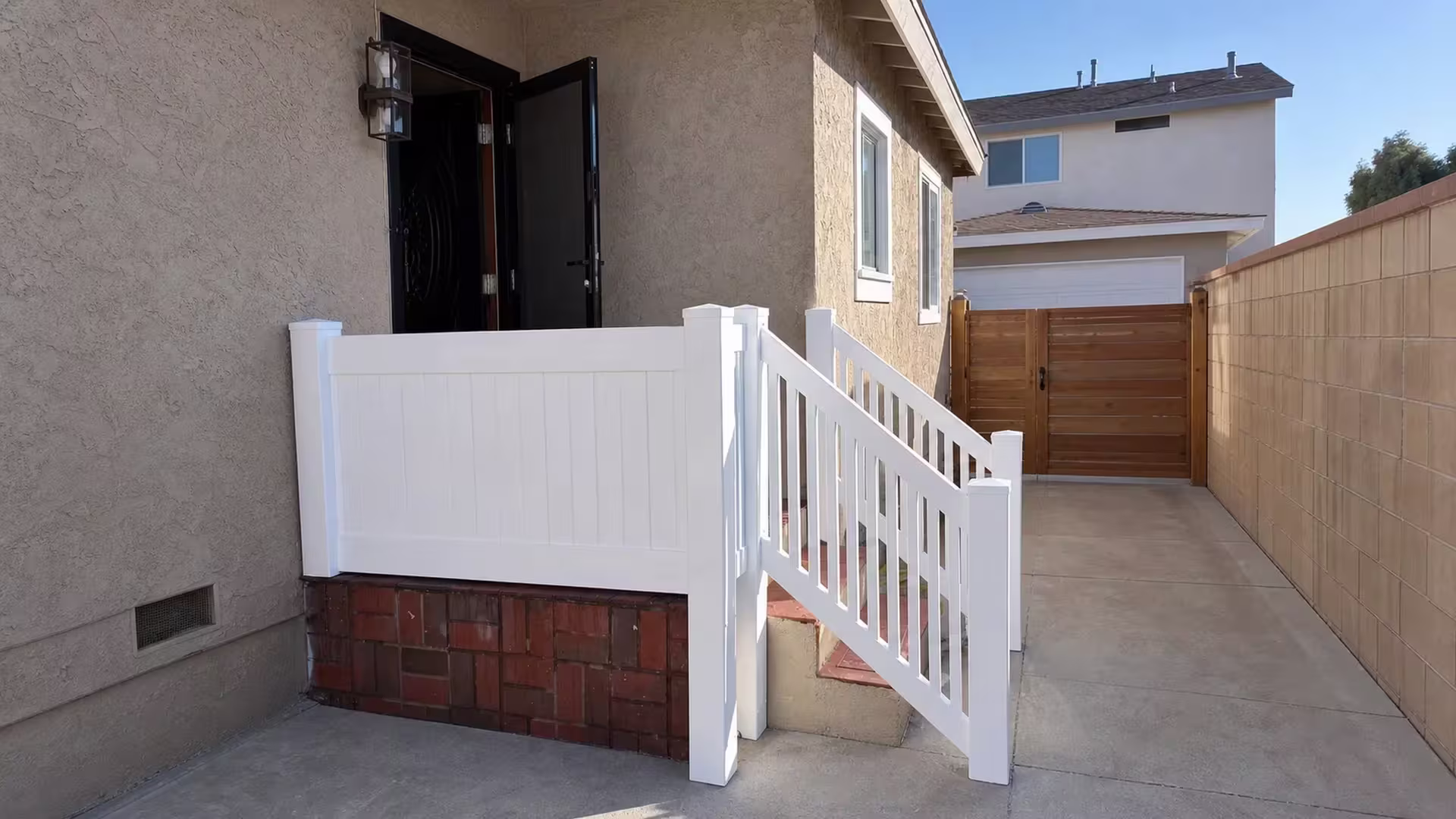A solid White vinyl privacy panel railing sits above a red brown brick base at the porch steps