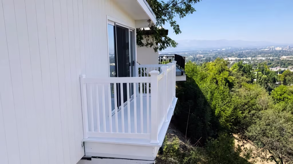 White vinyl balcony railing wraps a corner beside a dark sliding glass door with a hillside valley view