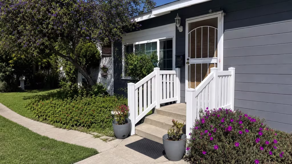 A security door and doormat sit beside White vinyl porch and landing railing at the entry