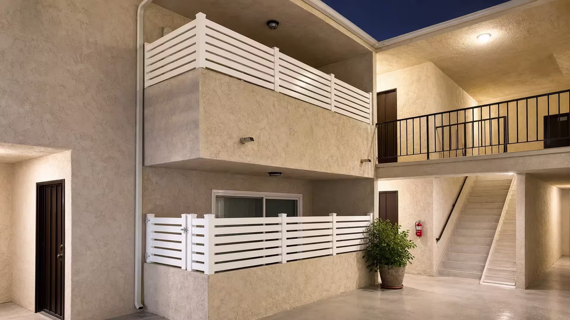 White vinyl open slat balcony railing turns a corner post near a wall mounted fire extinguisher