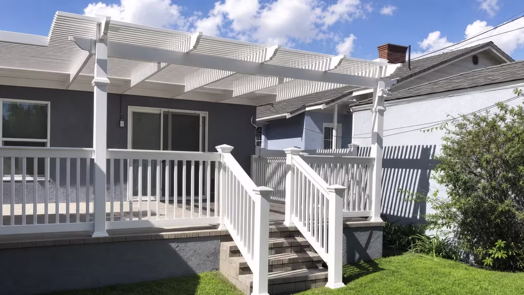 A louvered patio cover shades White vinyl porch railing flanking a tiled center stairway on a gray house