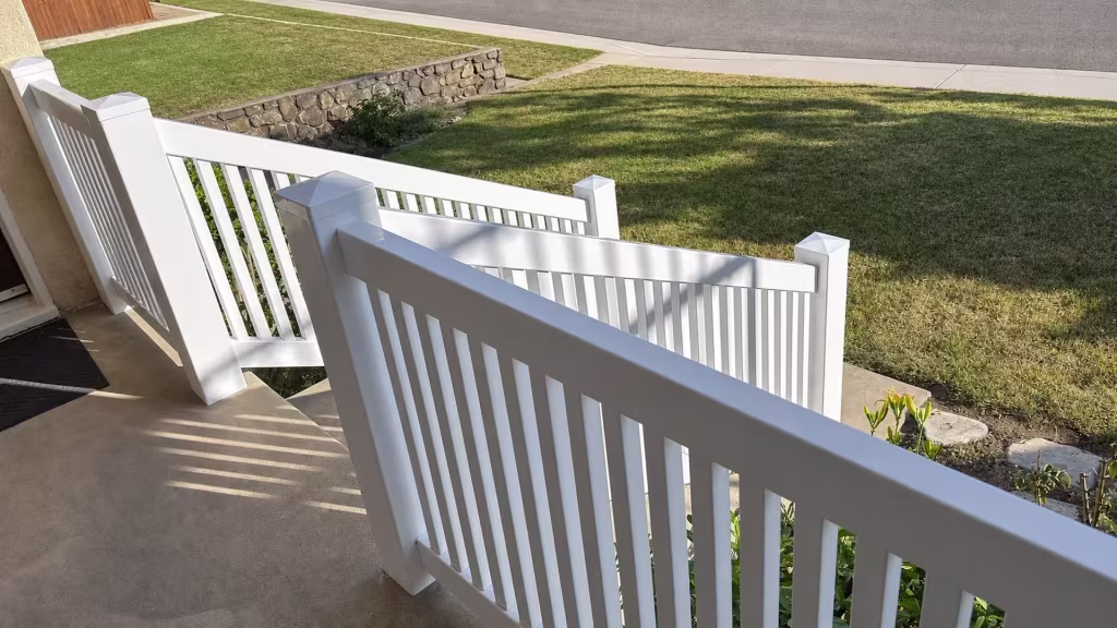 A stone retaining wall borders White vinyl porch and yard railing in four connected sections