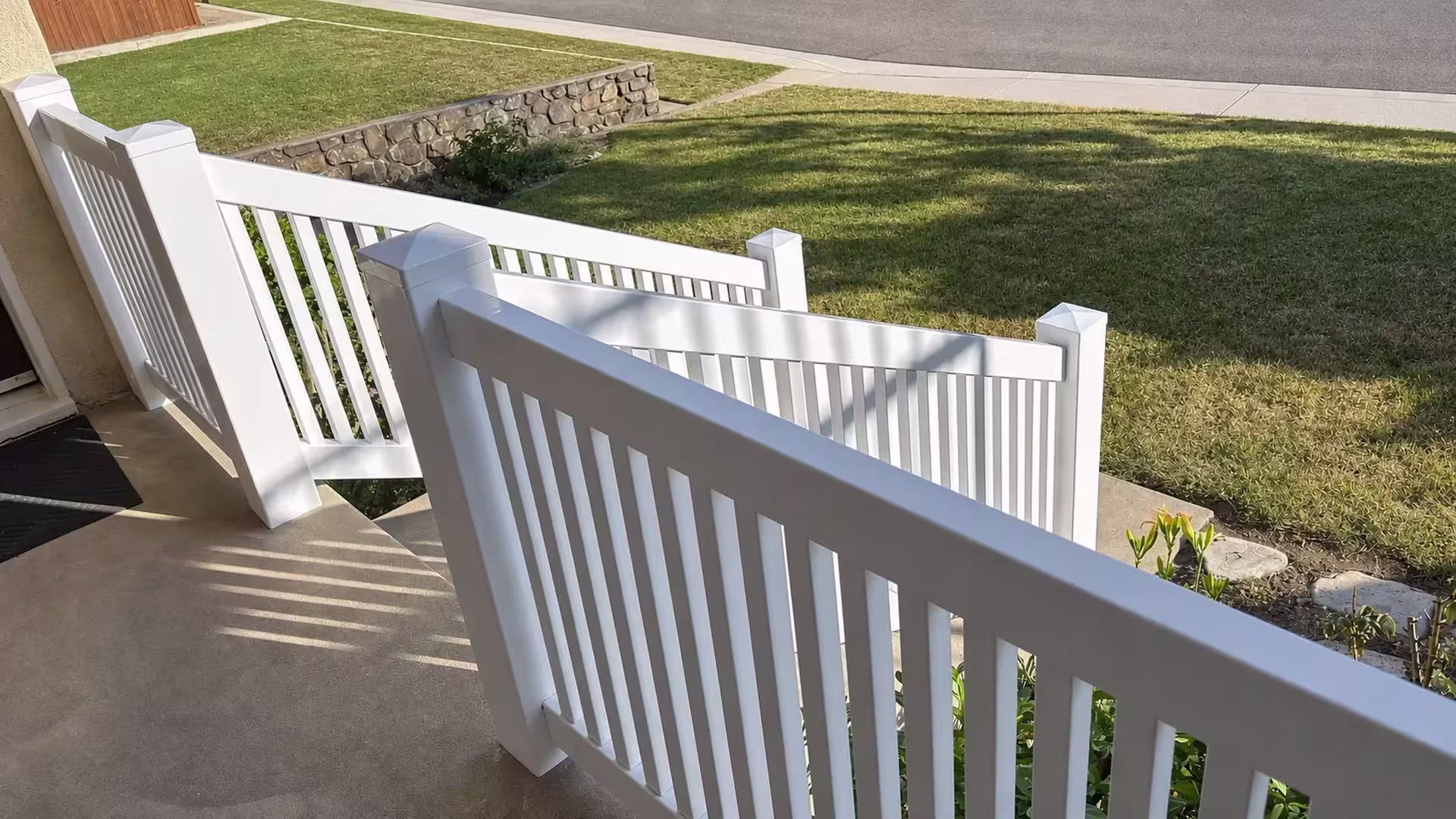A stone retaining wall borders White vinyl porch and yard railing in four connected sections