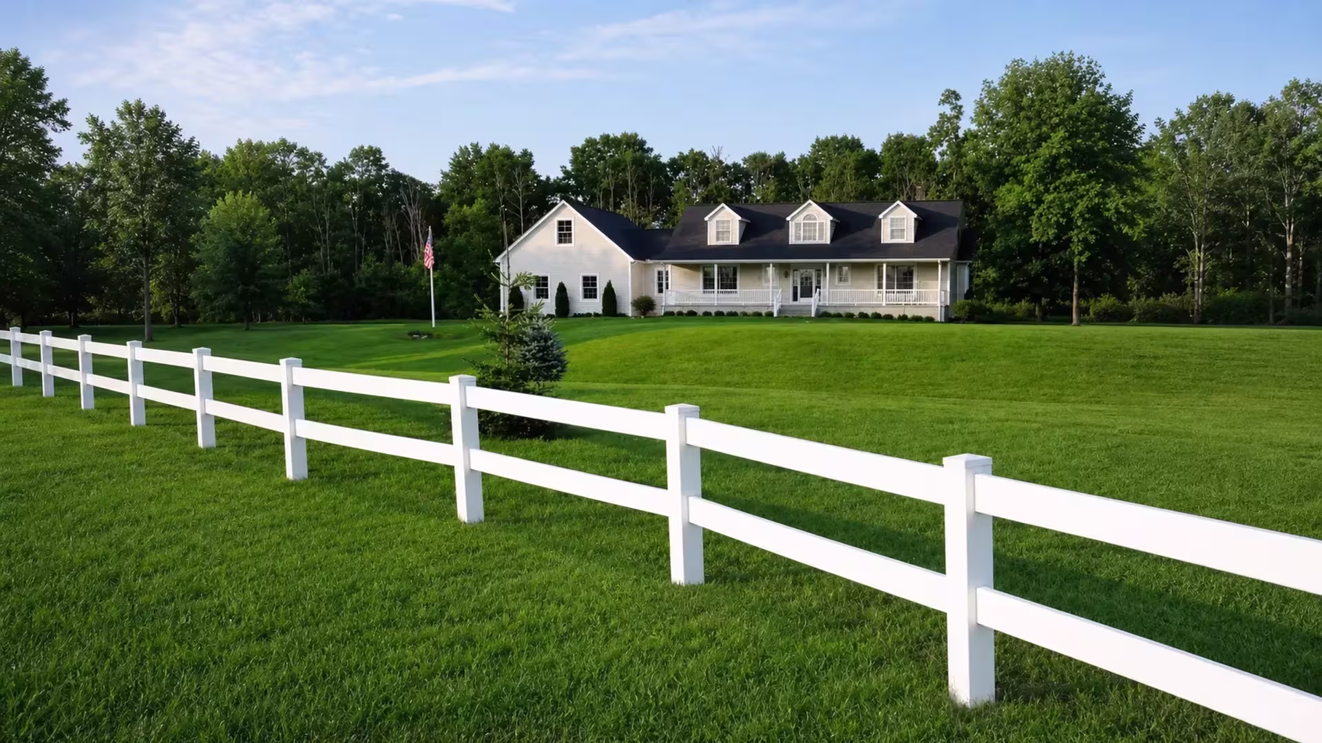 A ranch-style White vinyl fence with two rails crosses a lawn toward a dormered house