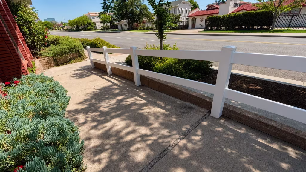 Beside a brick building, two White vinyl ranch rails frame a low planter wall