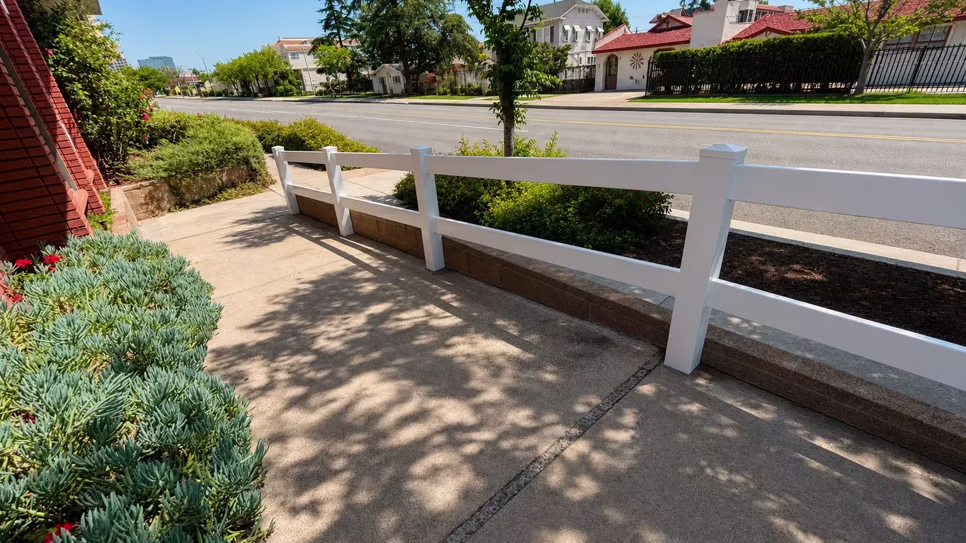 Beside a brick building, two White vinyl ranch rails frame a low planter wall