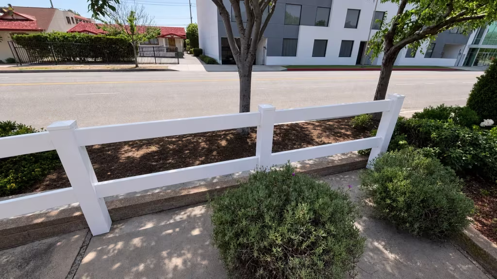 Three complete two-rail bays of White vinyl ranch fencing cross a sidewalk-lined foreground