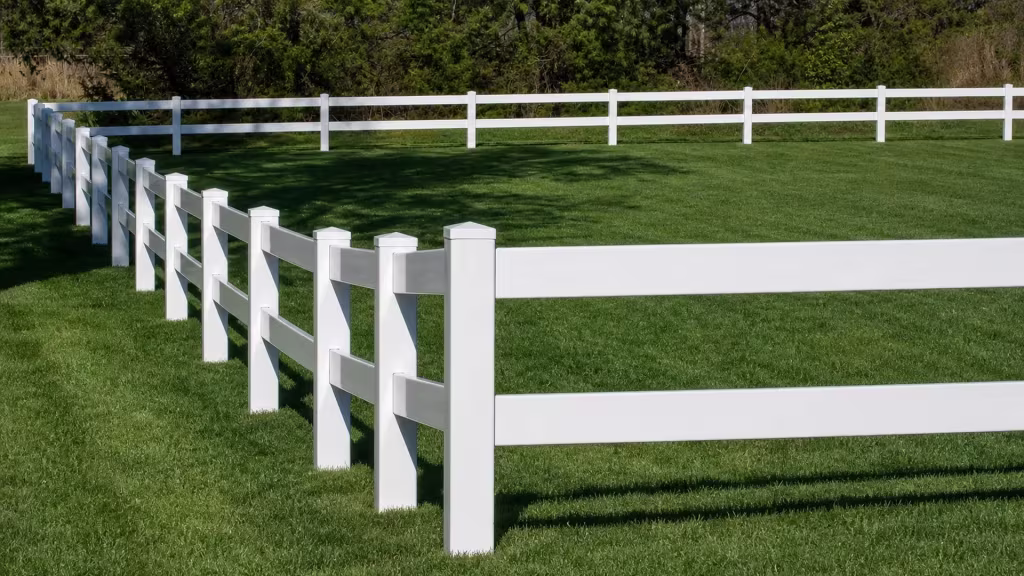 White vinyl ranch fencing forms two parallel two-rail runs across a grassy property