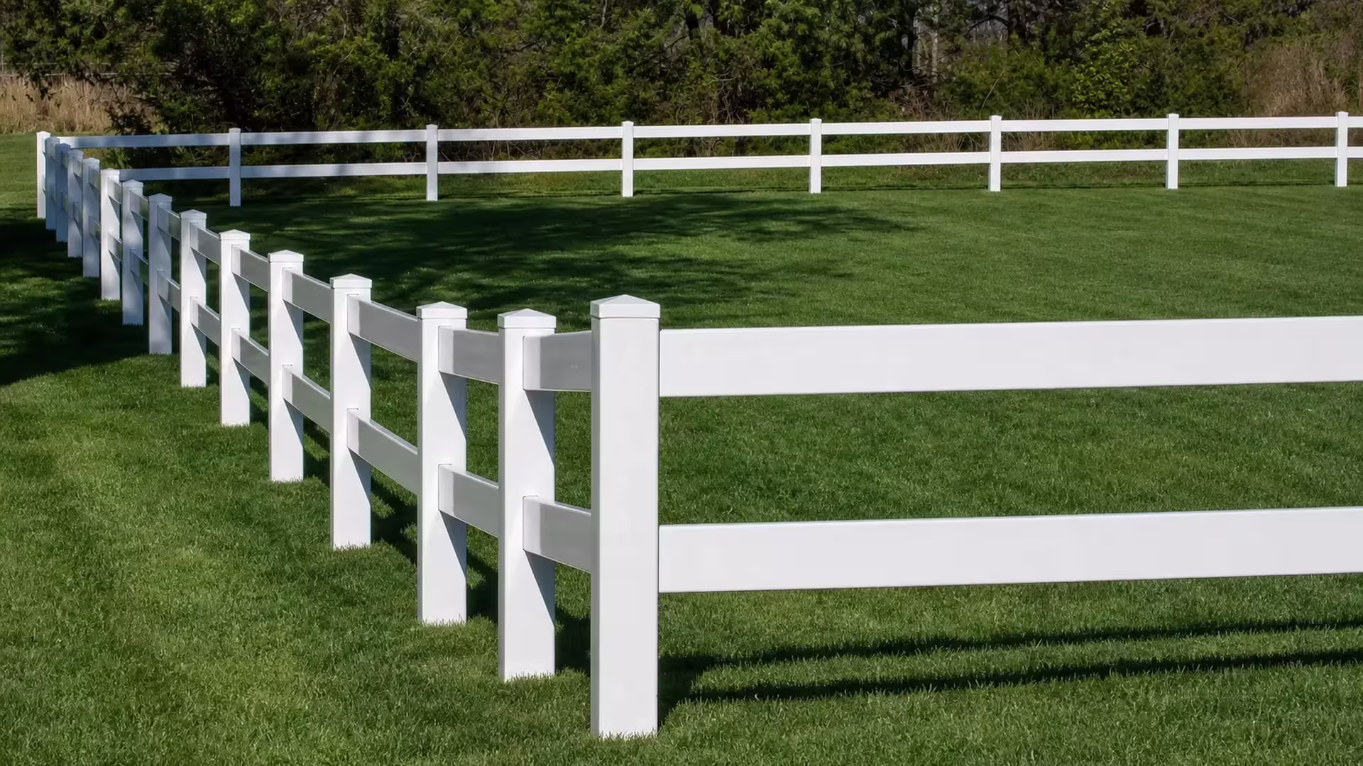 White vinyl ranch fencing forms two parallel two-rail runs across a grassy property