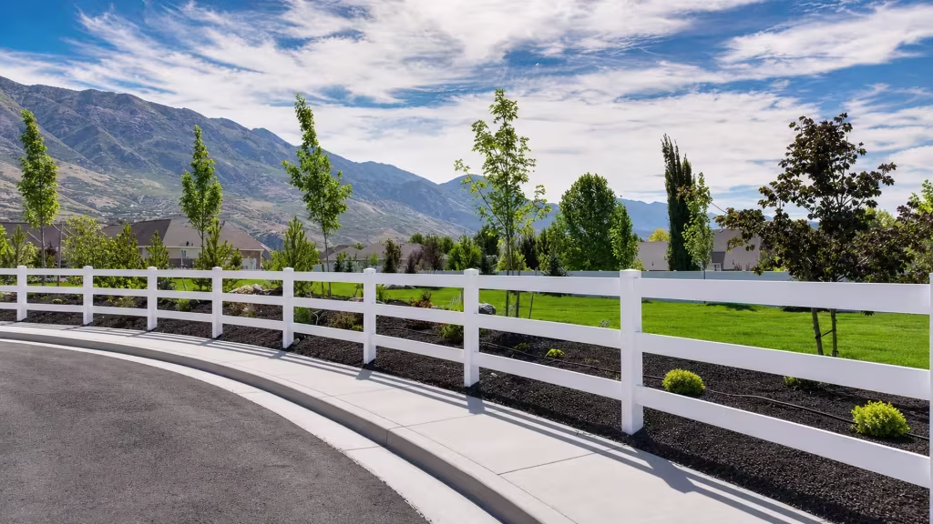 Long White vinyl ranch rail fence runs past a curved concrete walkway with a mulched planting bed alongside