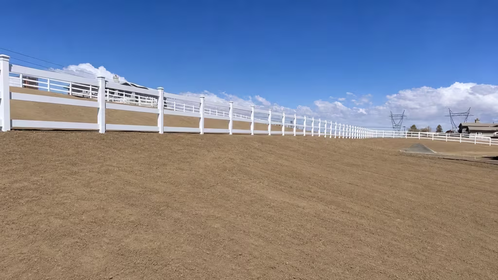 Open rail White vinyl ranch fence stretches across a graded dirt property beneath a line of utility towers