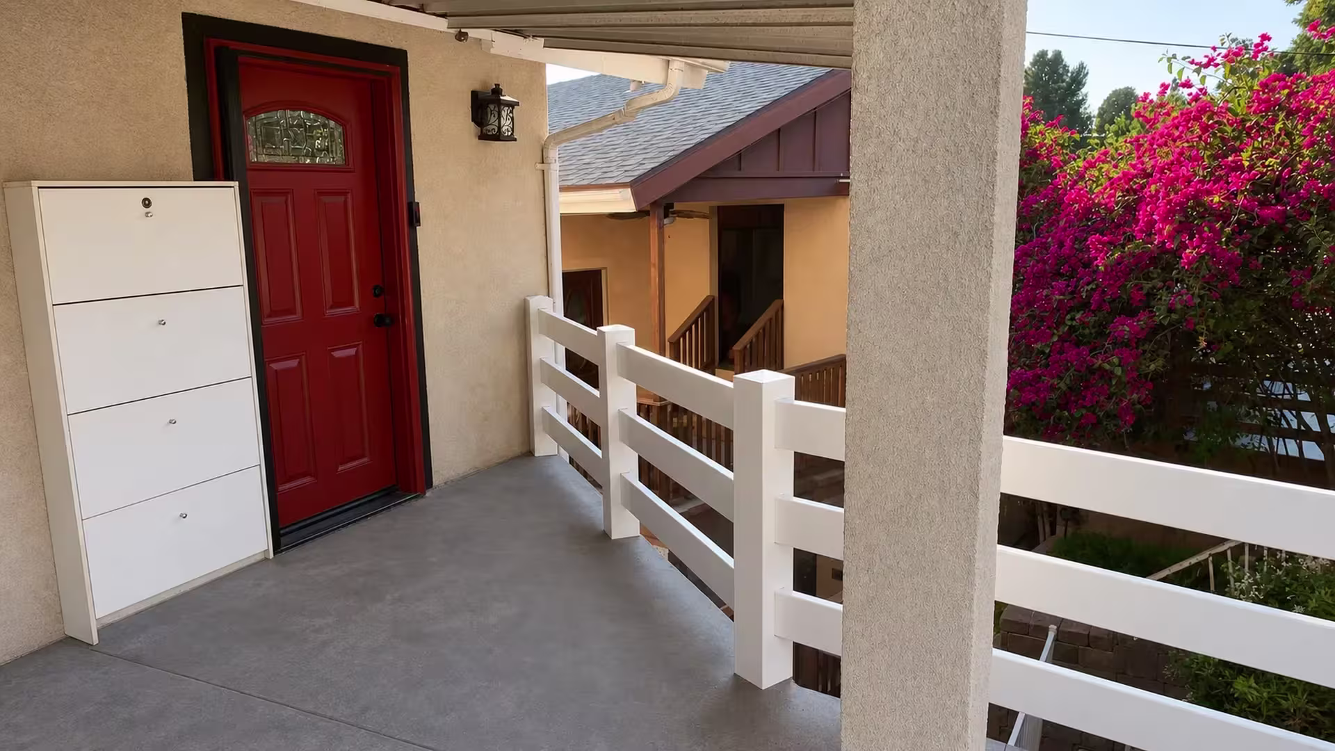 Wrapping an elevated concrete porch and stair, White vinyl ranch rail railing runs beside a red entry door