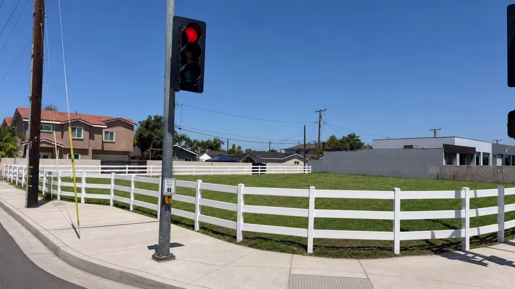 Enclosing a corner lot near curb ramps, this White vinyl ranch rail fence passes below overhead traffic signal wiring