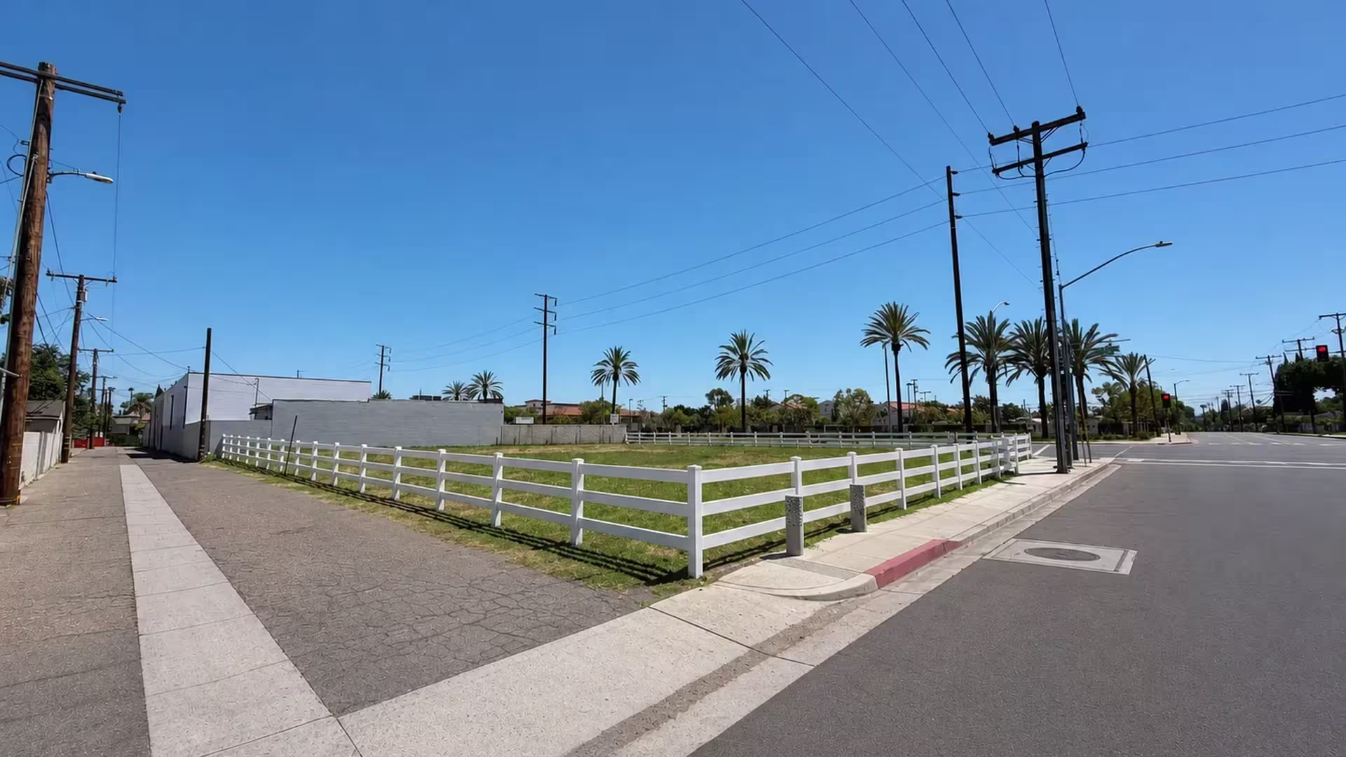 Continuous White vinyl ranch rail fence wraps two sides of a vacant urban lot at a right angle corner
