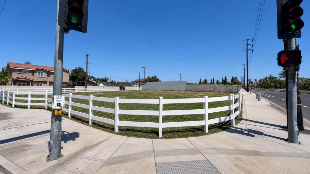 White vinyl ranch rail fence frames a corner lot right beside a curb ramp finished in tactile paving
