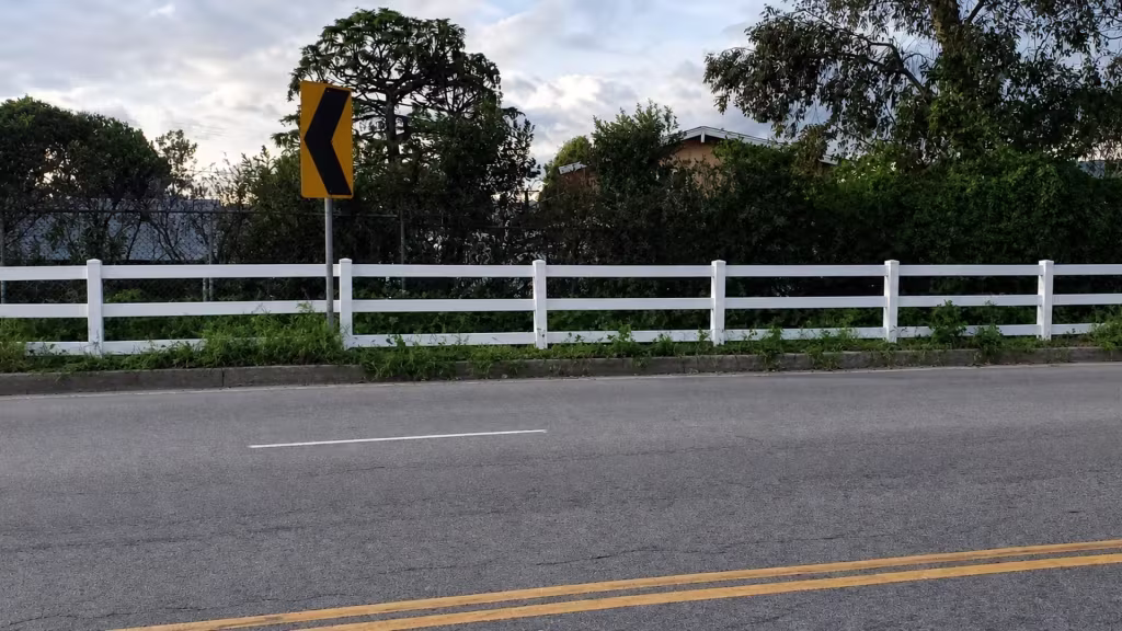 Seven fence posts carry this White vinyl ranch rail fence the length of a road marked by double yellow lines
