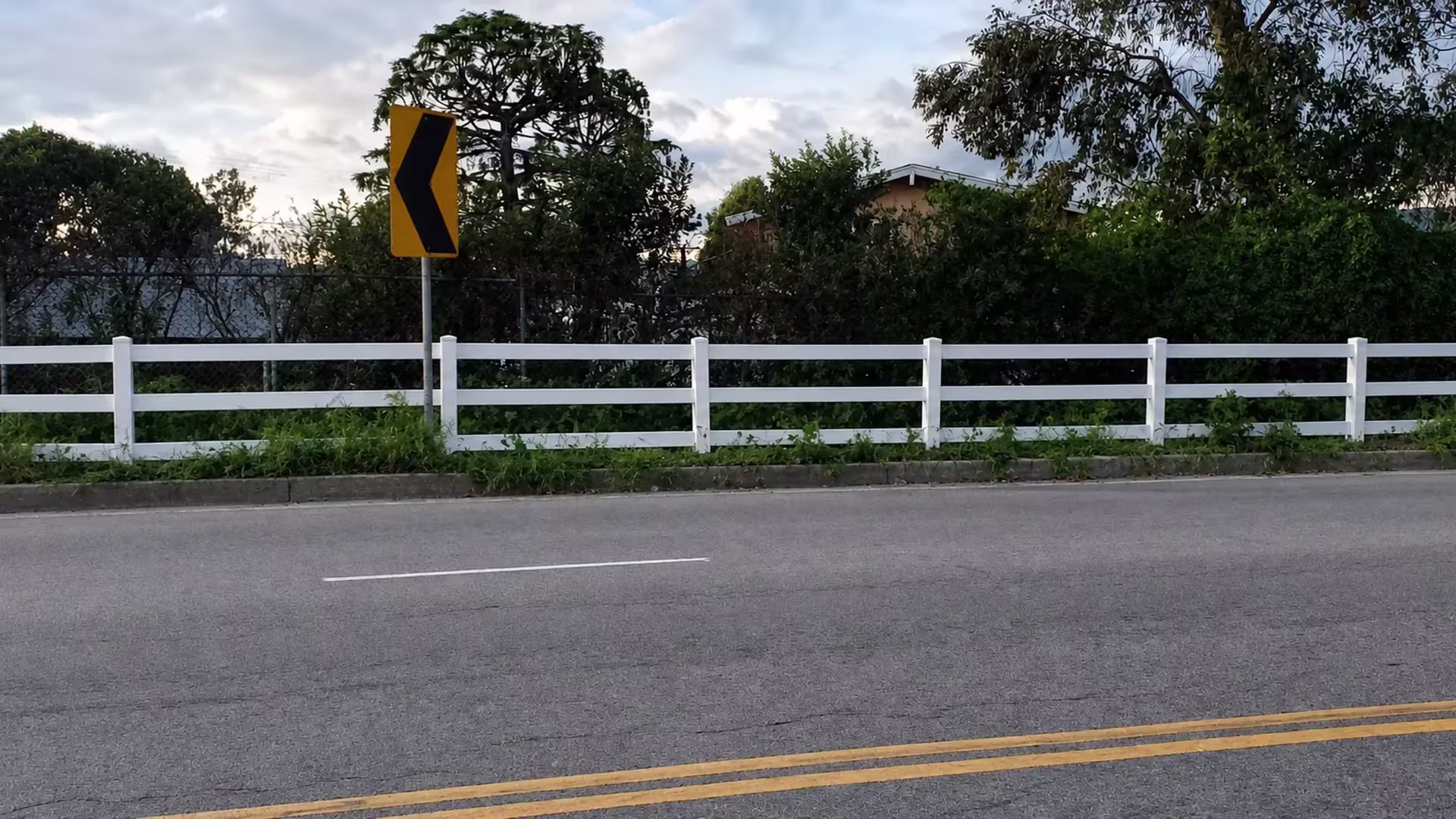 Seven fence posts carry this White vinyl ranch rail fence the length of a road marked by double yellow lines