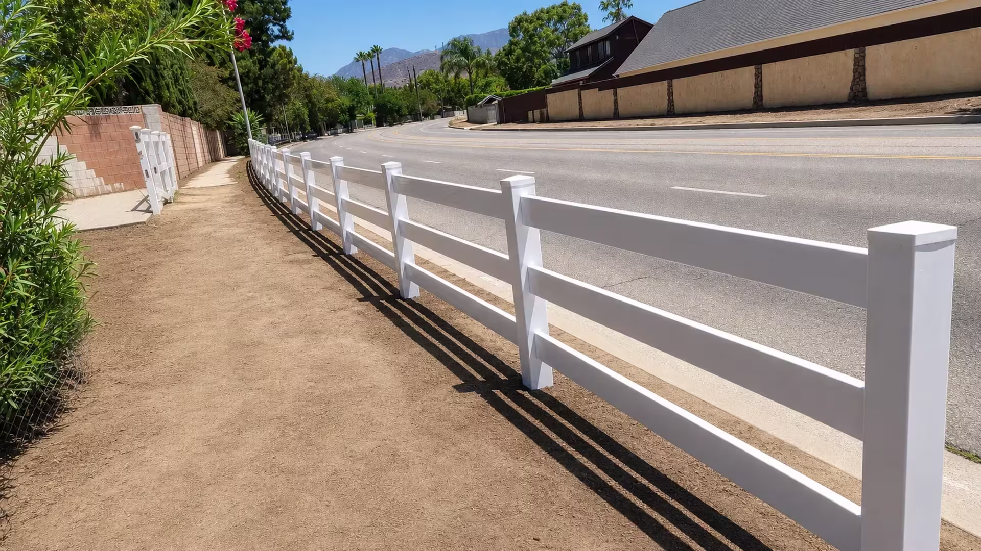 Newly installed, this three-rail White vinyl ranch fence follows a roadside sidewalk over graded soil