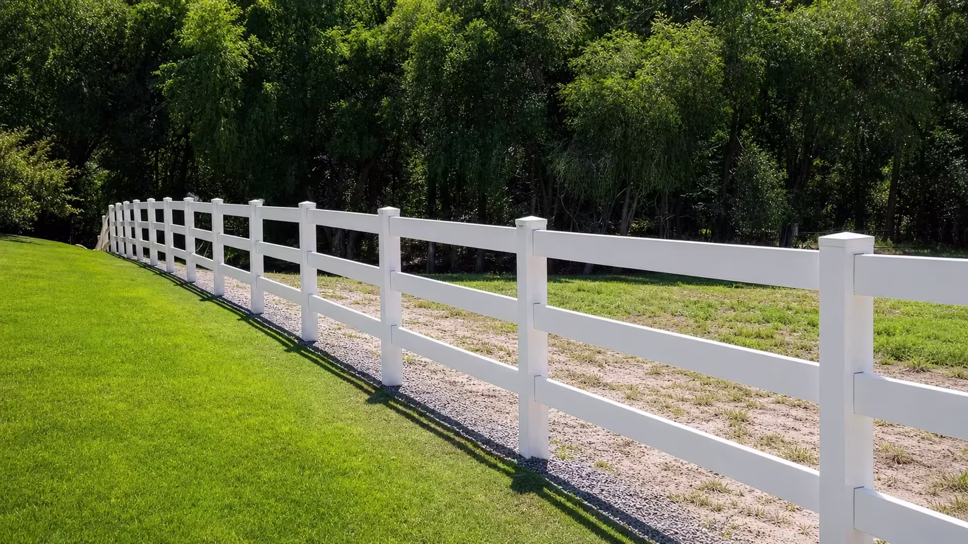 Ten visible posts and a narrow gravel strip accompany this White three-rail vinyl ranch fence beside a paddock