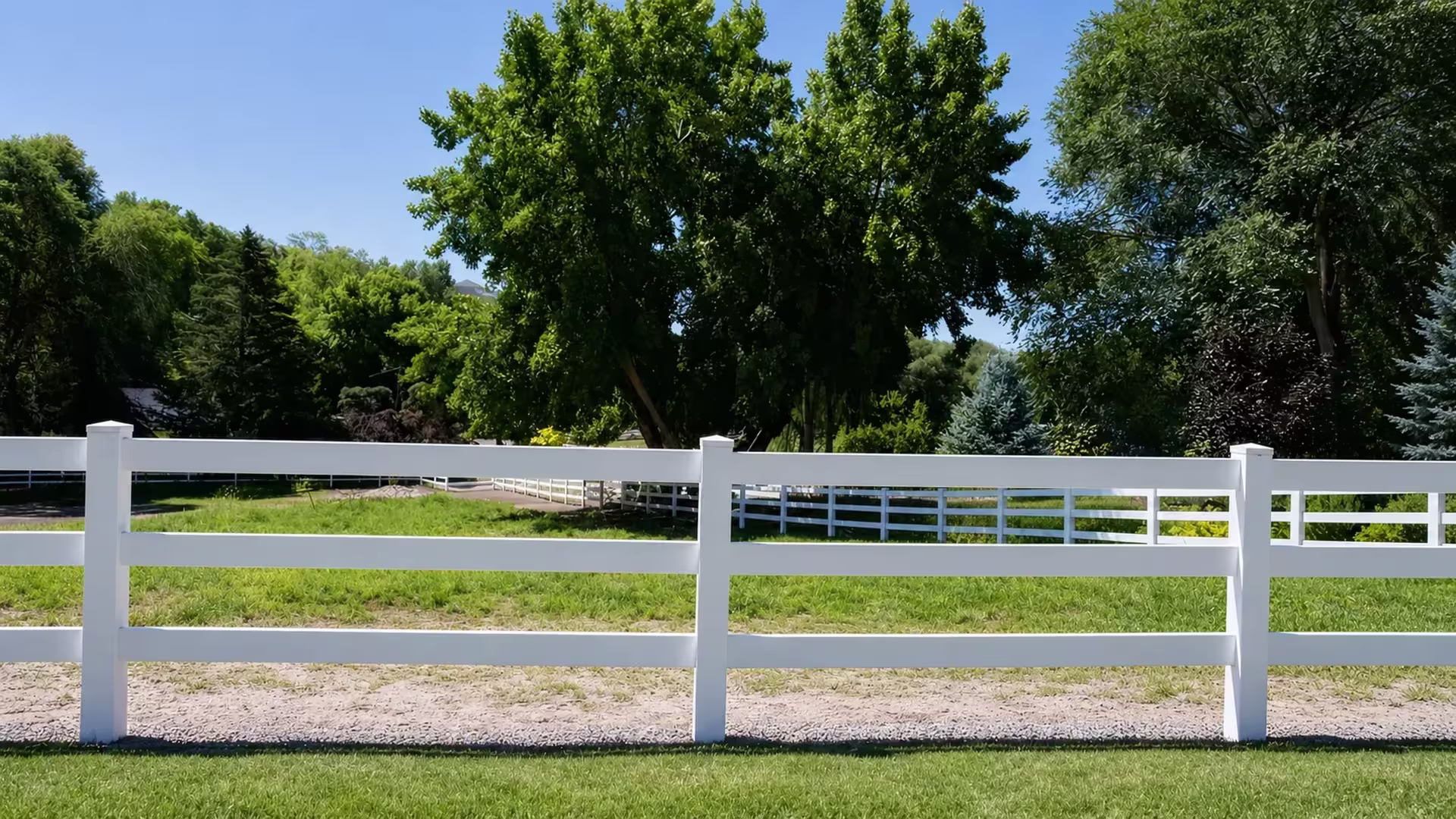 This White vinyl ranch fence crosses an open pasture on three rails, with matching fence runs visible in the distance