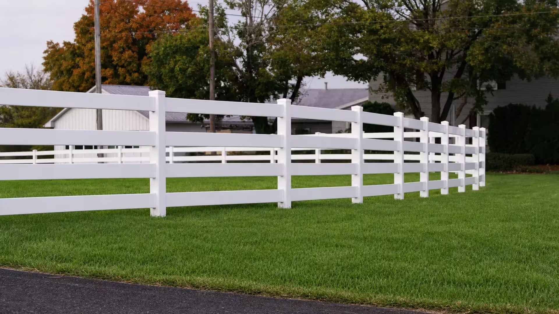 Nine visible posts carry this White vinyl fence, built with four ranch rails, diagonally across open grass near utility poles