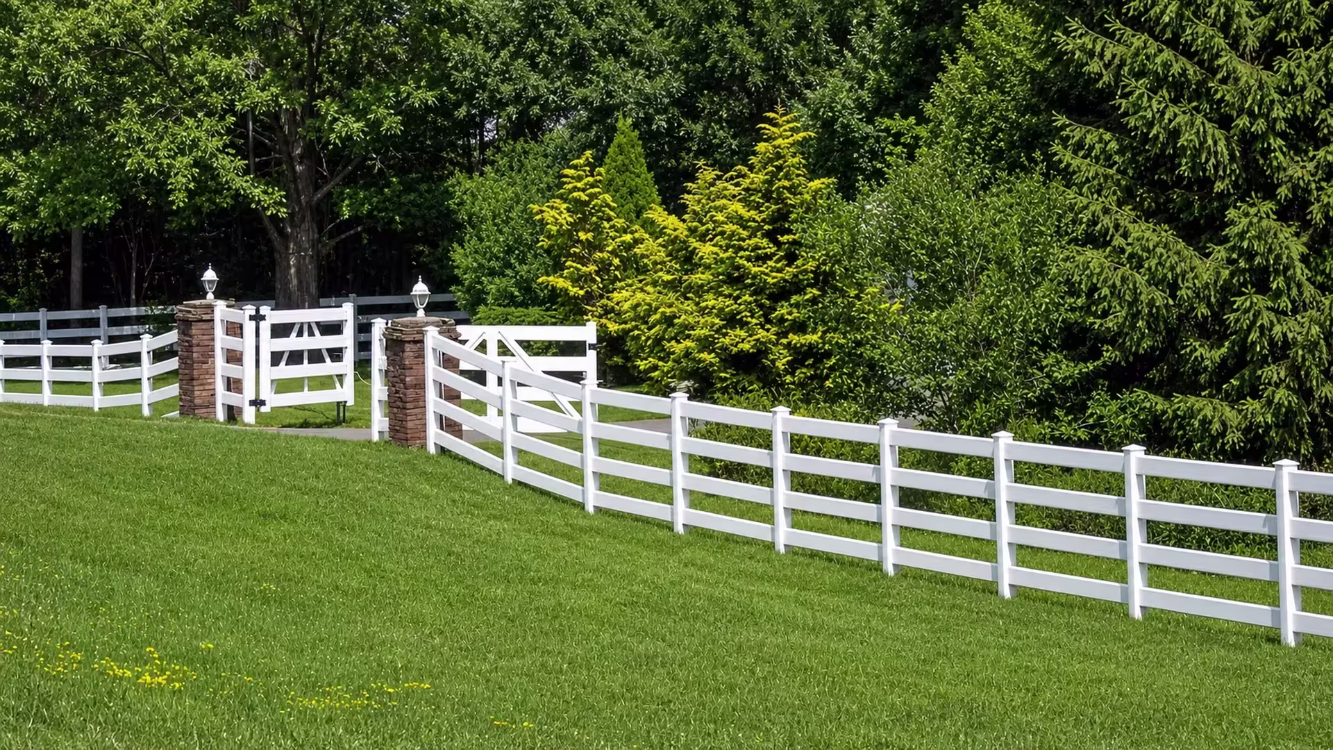 Beginning beside a stacked stone masonry column, this White vinyl ranch fence carries four rails down the sloping lawn