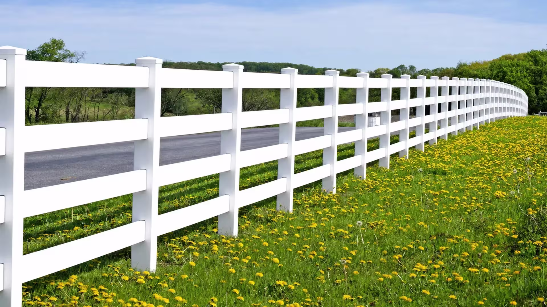 White vinyl four rail ranch fence follows a long, gentle curve into the distance