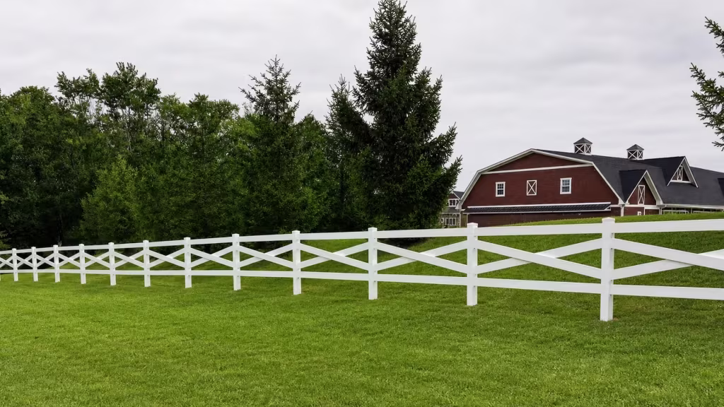 Diagonal White vinyl cross rails angle across a gently sloping stretch of lawn toward the right edge