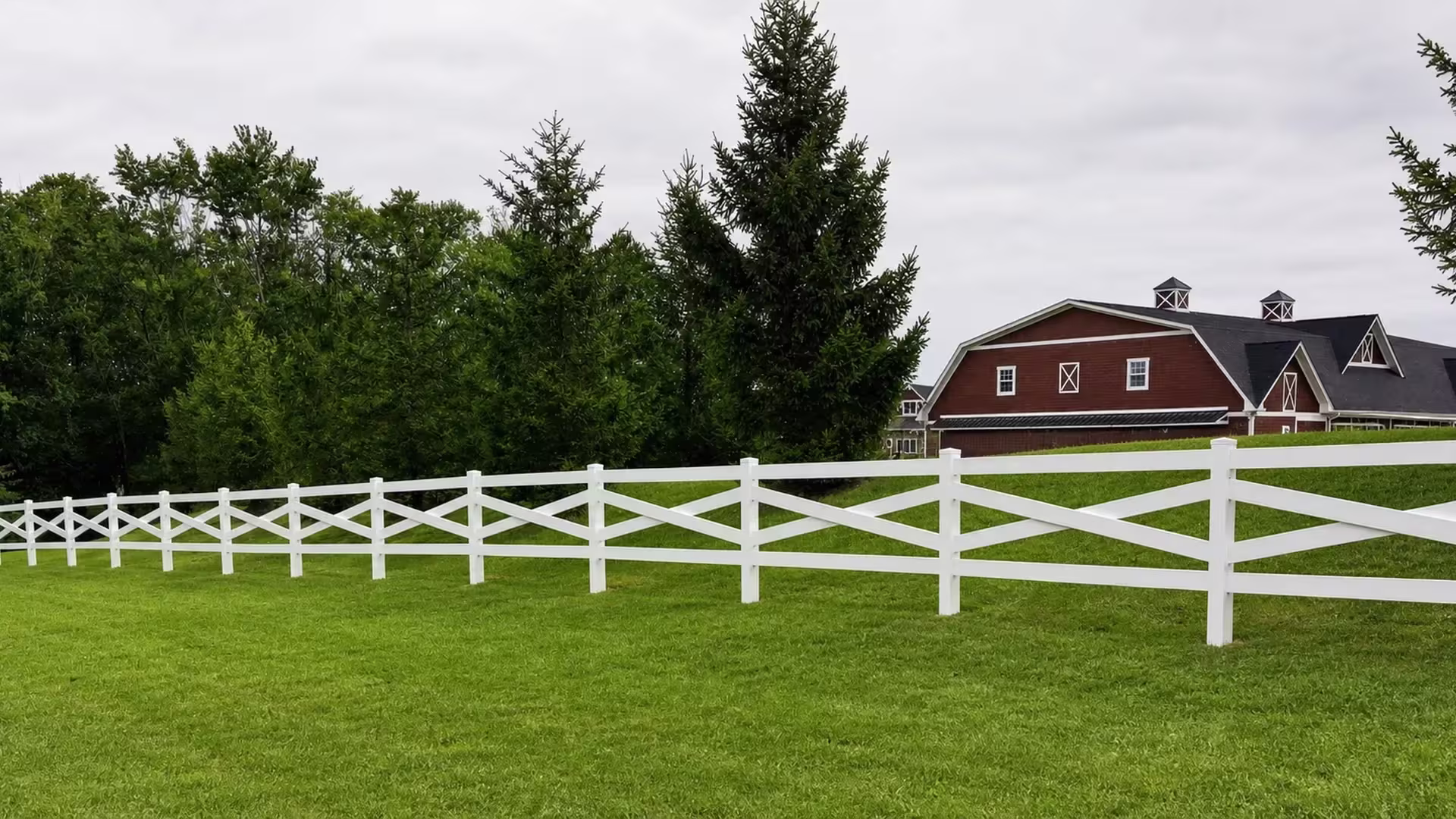 Diagonal White vinyl cross rails angle across a gently sloping stretch of lawn toward the right edge